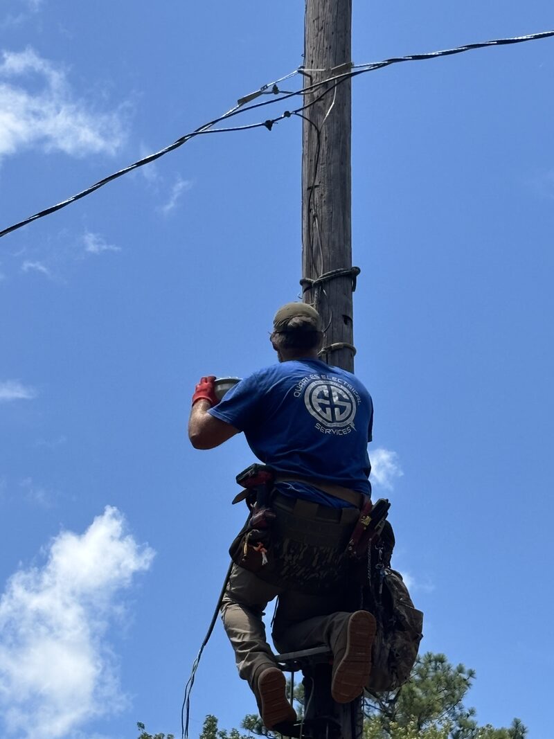 Quarles Electrical Services technician in a branded shirt working overhead on a utility pole
