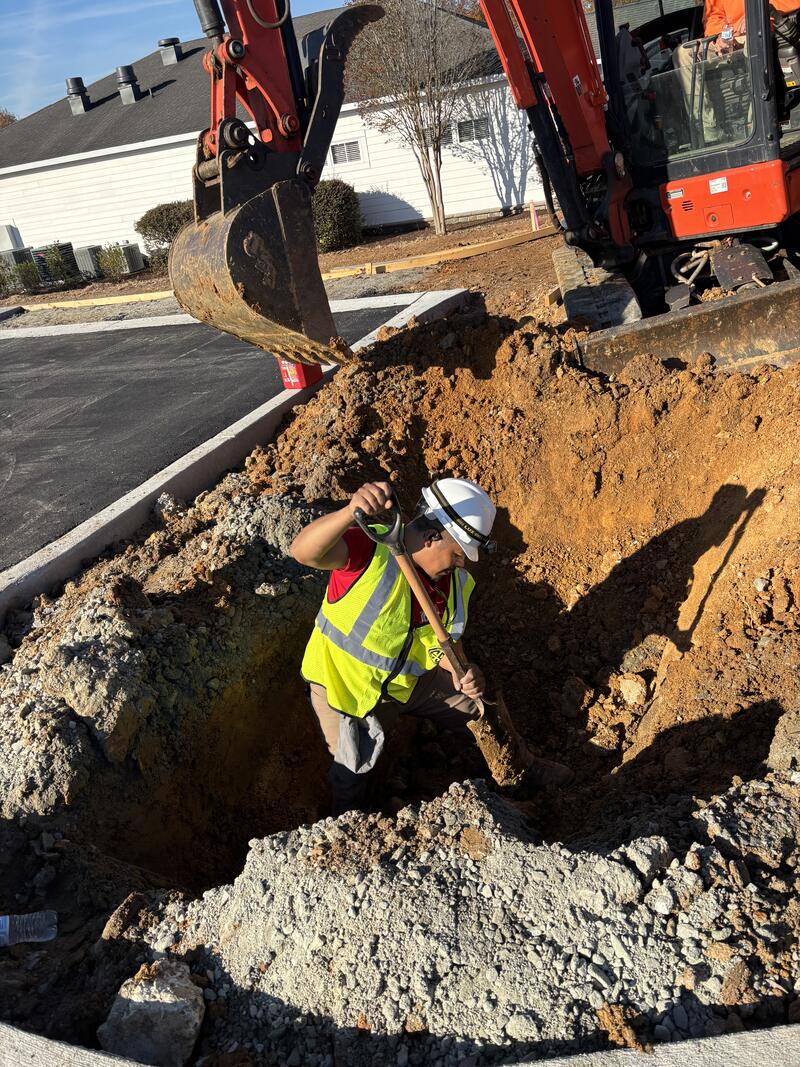 Crew trenching for underground electrical service beside a mini excavator